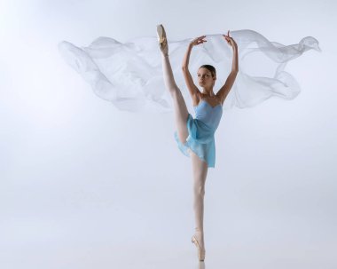 Genç bir kız, mavi elbiseli balerin olmak için can atıyor ve gri arka planda izole edilmiş kumaşla dans ediyor. Sanat, zarafet, güzellik, bale okulu konsepti