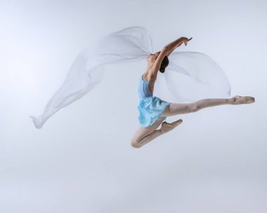 Genç bir kız, mavi elbiseli balerin olmak için can atıyor ve gri arka planda izole edilmiş kumaşla dans ediyor. Sanat, zarafet, güzellik, bale okulu konsepti