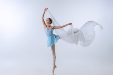 Güzel bir genç kız, mavi elbiseli ve gri arka planda izole edilmiş kumaşla dans eden hevesli bir balerin. Sanat, zarafet, güzellik, bale okulu konsepti