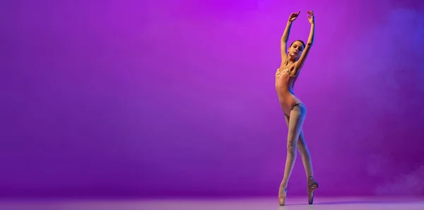 Krásná ohebná mladá baletka, dospívající v divadelním oblečku a pointes tanec izolovaný na purpurovém pozadí v neonovém světle s kouřem. Umění, půvab, krása. Oznámení — Stock fotografie