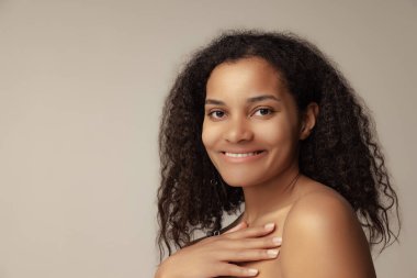 Gri arka planda izole edilmiş, doğal makyajlı, gülümseyen genç bir kadının yakın plan portresi. Güzellik kavramı