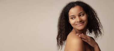 Gri arka planda izole edilmiş kıvırcık saçlı ve doğal görünüşlü güzel bir kadının yakın plan portresi.