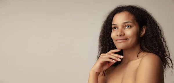 Close-up portrait of young beautiful woman with natural makeup and curly hair posing isolated over grey background — стоковое фото