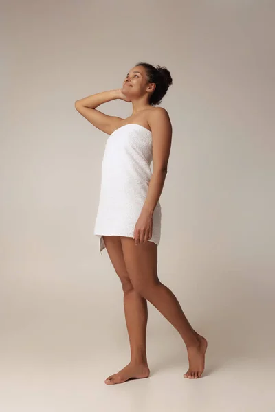Полнометражный портрет молодой красивой женщины, позирующей в белом полотенце, изолированный на сером фоне студии — стоковое фото