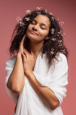 Beyaz bornozlu güzel bir kadının portresi pembe stüdyo arka planında izole bir şekilde poz veriyor. Doğal güzellik konsepti