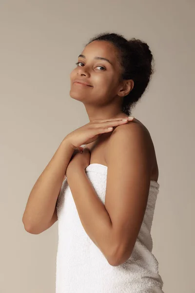 Полудлинный портрет молодой нежной женщины в белом полотенце, позирующей, смотрящей на камеру изолированной на сером фоне студии — стоковое фото
