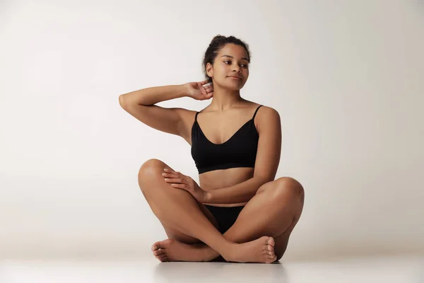 Portrait of young beautiful woman sitting on floor, posing in black underwear isolated over gray backgoround. Female health care —  Fotos de Stock