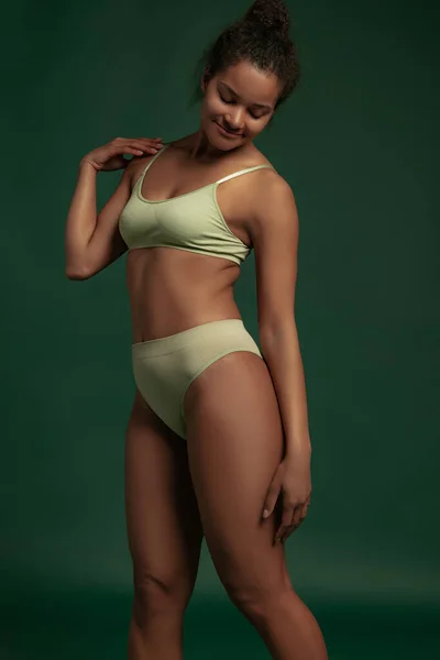 Portrait of young woman posing in underwear isolated over green studio background. Anti-cellulite concept — стоковое фото