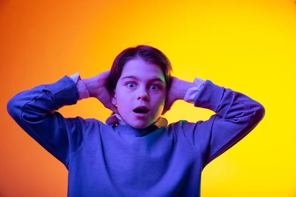 Ritratto di ragazzo, bambino che mette le mani dietro la testa con espressione scioccata isolato su sfondo giallo studio al neon — Foto Stock