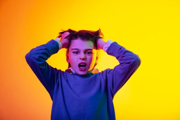 Ritratto di ragazzo emotivo, bambino che tocca i capelli in irritazione, rabbia isolata su sfondo giallo studio in luce al neon — Foto Stock