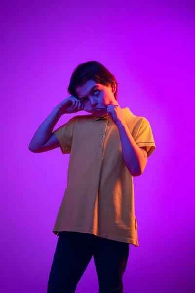 Portret van grappige jongen, kind maken griezelige gezichten, plezier hebben, poseren geïsoleerd over paarse achtergrond in neon licht — Stockfoto