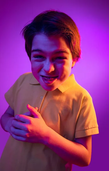 Portrait of boy, child, making faces, smirking isolated over purple background in neon light — Stock Photo, Image