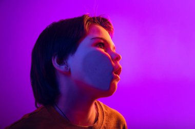 Yakın plan çocuğu, şeffaf cama yanak yanağa yaslanan çocuk neon ışıklarıyla izole edilmiş mor stüdyoda. Komik surat.