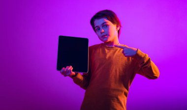 Çocuğun portresi, tableti işaret eden çocuk mor arkaplan üzerinde izole edilmiş neon ışıkta