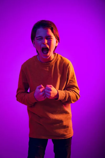 Retrato de menino emotivo, criança gritando, gritando isolado sobre fundo roxo em luz de néon — Fotografia de Stock