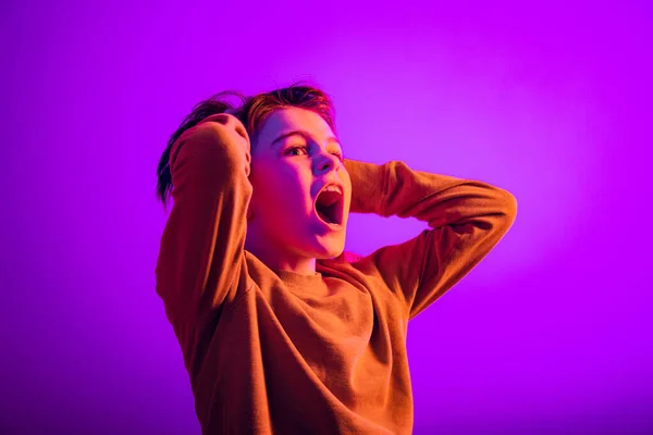 Portré fiú, gyermek fogja a kezét a feje mögött, és kiabál elszigetelt lila háttér neon fény — Stock Fotó