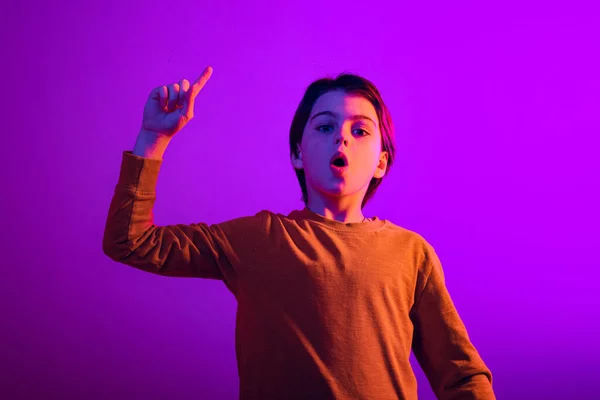 Portrét chlapce, dítě zvedající prst, s novou myšlenkou izolované přes fialové pozadí studia v neonovém světle — Stock fotografie