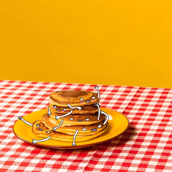 Food pop art photography. Plate with pancakes with funny drawings on plaid tablecloth isolated on bright yellow background. Cartoon, vintage, retro style — Stock Photo, Image