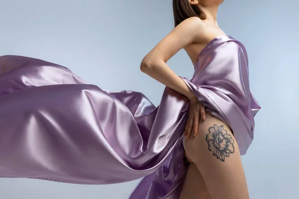 Обрізаний студійний знімок тонкого жіночого тіла, покритого фіолетовою шовковою тканиною, ізольовано на синьому студійному фоні — стокове фото