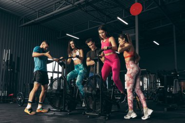 Spor yapan bir grup genç arkadaş, spor salonunda antrenman yapıyorlar. Egzersiz bisikletinde kadın eğitimi. Bacak antrenmanı günü.