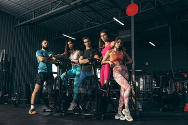 Spor yapan bir grup genç arkadaş, spor salonunda antrenman yapıyorlar. Egzersiz bisikletinde kadın eğitimi