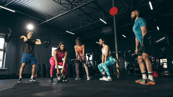 Grupp av unga vänner som idrottar, tränar på gym inomhus, gör benträning med vikt — Stockfoto