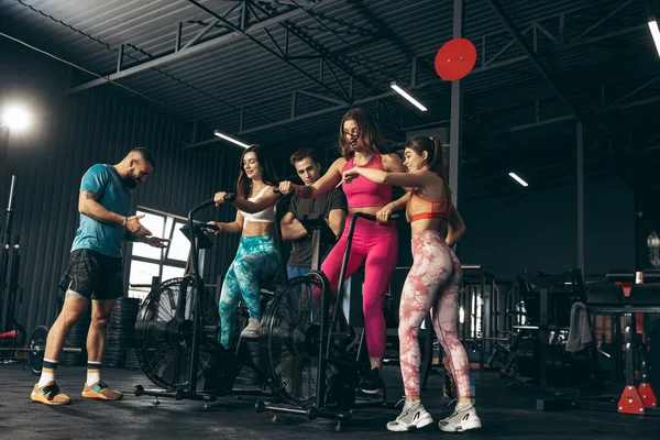 Grupa młodych przyjaciół uprawiających sport, trenujących na siłowni w pomieszczeniach. Trening kobiet na rowerze treningowym — Zdjęcie stockowe