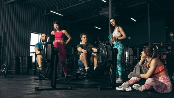 Spor yapan bir grup genç arkadaş, spor salonunda antrenman yapıyorlar. Çocuklar kürek çekme makinesinde egzersiz yapıyor. Yağ yakma işi.