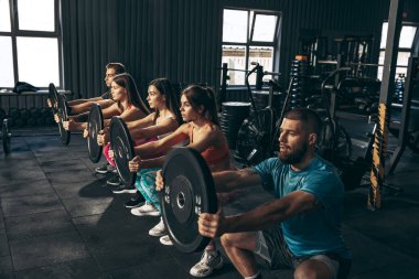 Spor yapan bir grup genç arkadaş, spor salonunda antrenman yapıyorlar. Ağırlıklarla çömelmek