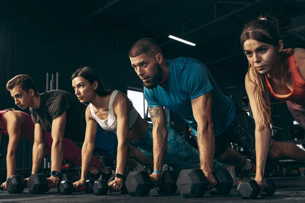 Grupa młodych przyjaciół uprawiających sport, trenujących na siłowni w pomieszczeniach. Stojąc na desce z hantlami — Zdjęcie stockowe