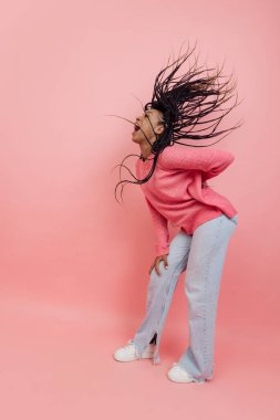 Stüdyo çekimlerinde, pembe arka planda izole edilmiş, afro saçlı, rahat görünümlü, eğlenceli genç bir kız vardı. Güzellik, sanat, moda, gençlik, tarz kavramı
