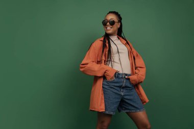 Koyu yeşil arka planda izole edilmiş şortlu ve gömlekli kadın manken portresi. Güzellik, sanat, moda, gençlik ve duygu kavramı