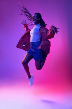 Studio shot of young excited woman in casual style outfit jumping isolated on purple background. Concept of beauty, art, fashion, youth, style