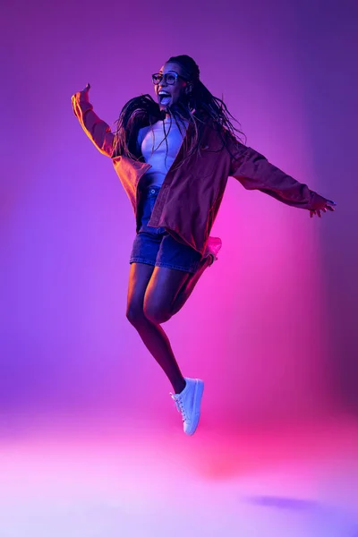 Studio shot of young excited woman in casual style outfit jumping isolated on purple background. Concept of beauty, art, fashion, youth, style — 스톡 사진