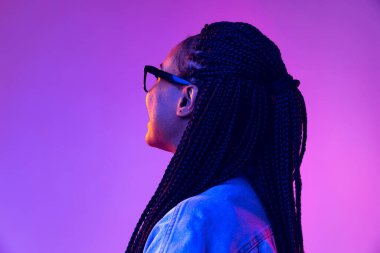 Mor arka planda, neon ışıkta izole edilmiş, afro saçlı genç bir kız. Güzellik, sanat, moda, gençlik ve duygu kavramı