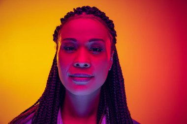 Closeup portrait of calm girl looking at camera isolated on yellow pink background in neon light. Concept of beauty, art, fashion, youth and emotions
