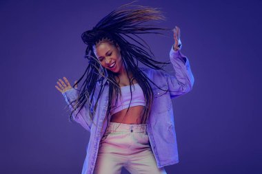 Emotional african girl in jeans and shirt dancing, having fun isolated on dark blue background. Concept of beauty, art, fashion, youth and emotions