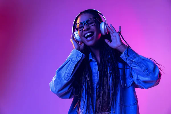 Music. Beautiful girl in headphones listening to music isolated on purple background in neon light. Concept of beauty, art, fashion, youth and emotions — Zdjęcie stockowe