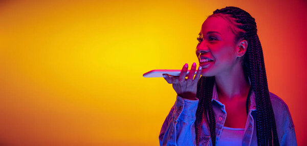 Young pretty girl in cotton shirt using phone isolated on yellow red background in neon light. Concept of beauty, art, fashion, youth and emotions