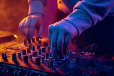 Neon ışıklarda yakın plan görüntü. Erkek eller profesyonel DJ mikserinde ses çıkarıyor. Canlı performans