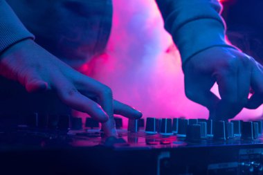 Neon ışıklarda yakın plan görüntü. Erkek eller profesyonel DJ mikserinde ses çıkarıyor. Yaratıcı ses düzenleyici