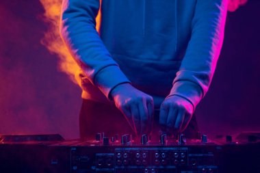 Neon ışıklarda yakın plan görüntü. Erkek eller profesyonel DJ mikserinde ses çıkarıyor. Tütsüleme etkisi