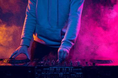 Duman efektli neon ışıklarda yakın plan görüntü. Erkek eller profesyonel DJ mikserinde sesleri çeviriyor