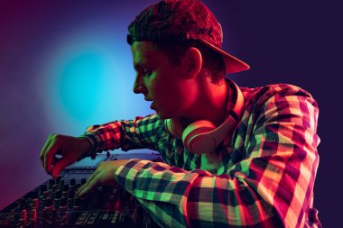 Günlük giysiler içinde genç bir çocuğun portresi, parti DJ 'i profesyonel ses mikseriyle müzik yapıyor mor arka planda, neon ışıkta izole edilmiş.