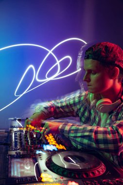 Günlük giysiler içinde genç bir çocuğun portresi, parti DJ 'i profesyonel ses mikseriyle müzik yapıyor mor arka planda, neon ışıkta izole edilmiş.