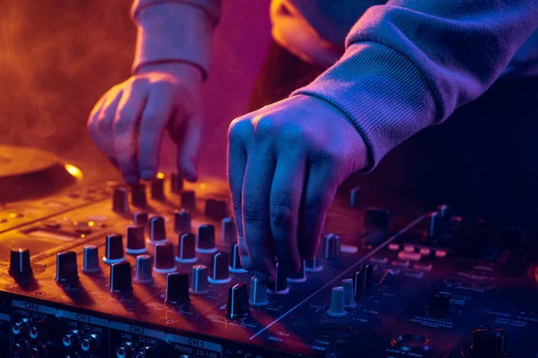 Close-up image in neon lights. Male hands turning sounds on professional dj mixer. Live performance — Foto de Stock