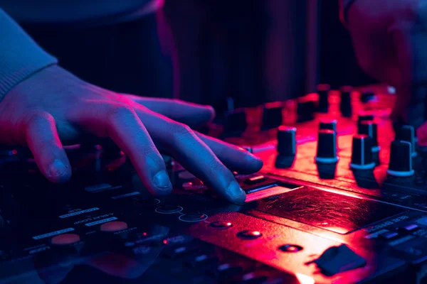 Imagen de cerca en luces de neón. Manos masculinas girando sonidos en mezclador dj profesional. Haciendo sonidos más fuertes y profundos — Foto de Stock