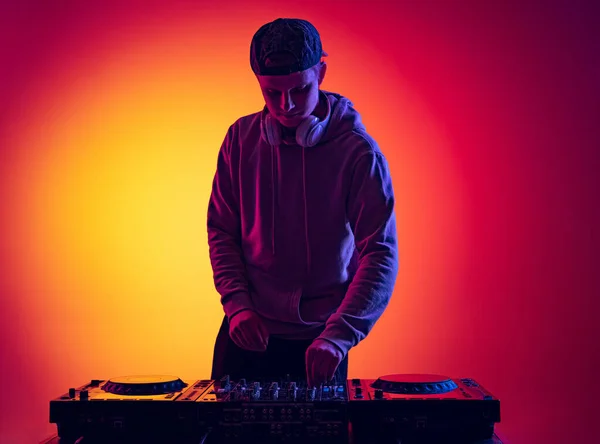 Porträtt av ung man att göra ljud med professionell dj mixer isolerad över lutning röd gul bakgrund i neon ljus — Stockfoto