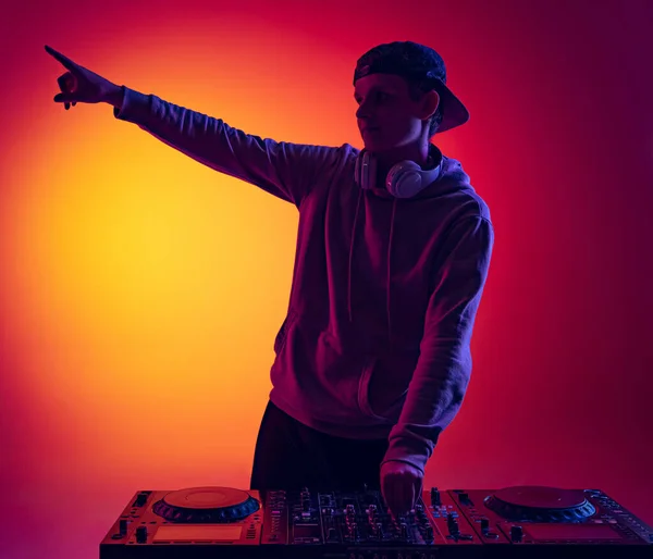 Porträtt av ung man, dj spela musik med speciell mixer på nattklubb, vilket gör partiet isolerad över lutning röd gul bakgrund i neon — Stockfoto