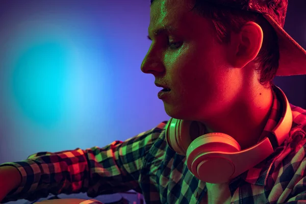 Close-up portrait of young boy with headphones making sounds with professional dj mixer isolated over blue background in neon lights — Stockfoto